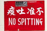 A red sign on a white wall reads 'no spitting' in Chinese and English