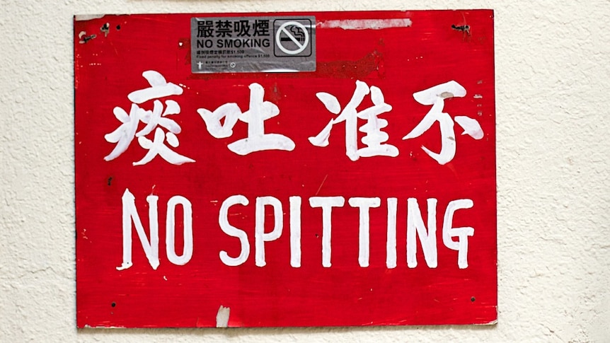 A red sign on a white wall reads 'no spitting' in Chinese and English
