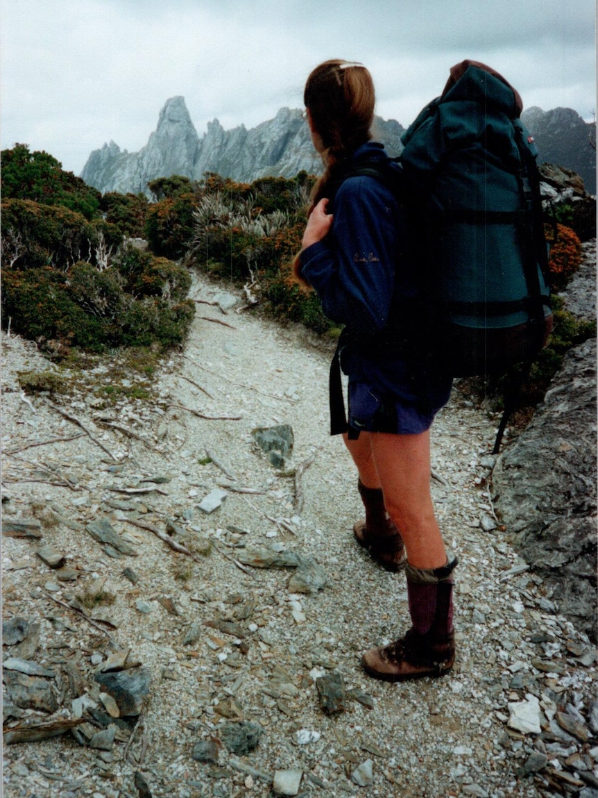 a woman in hiking gear looks ahead at a large rocky mountain