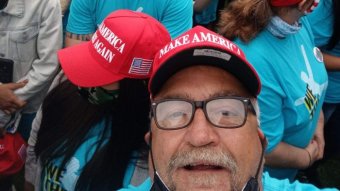 A man in a MAGA cap looks at the camera as he takes a selfie in a crowd