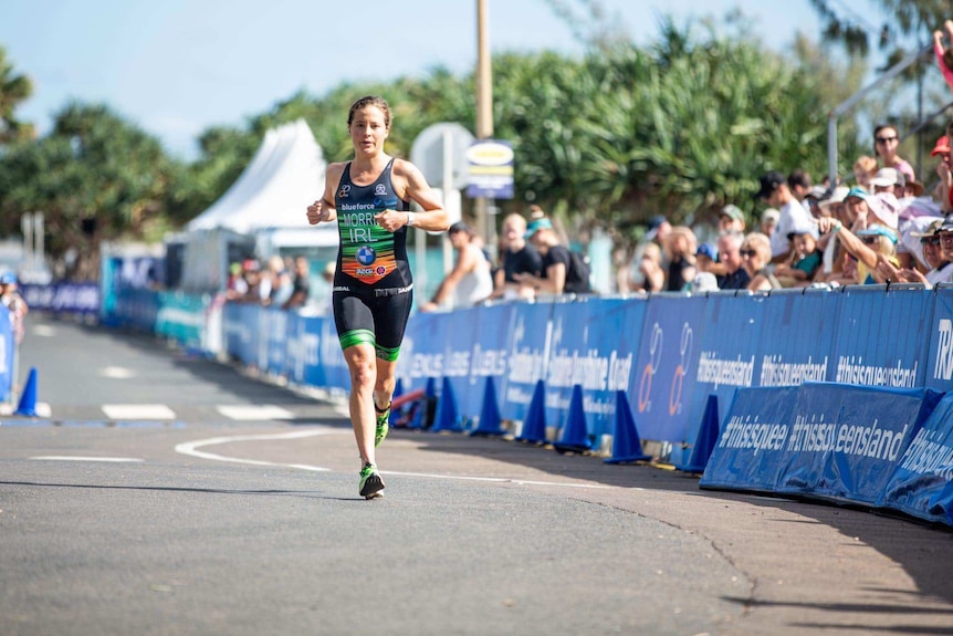 Woman wearing a black and green triathlon suit runs on a road