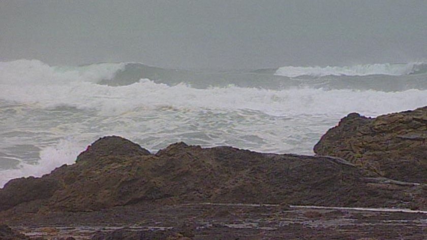 Rough seas crashing on rocks on beach.