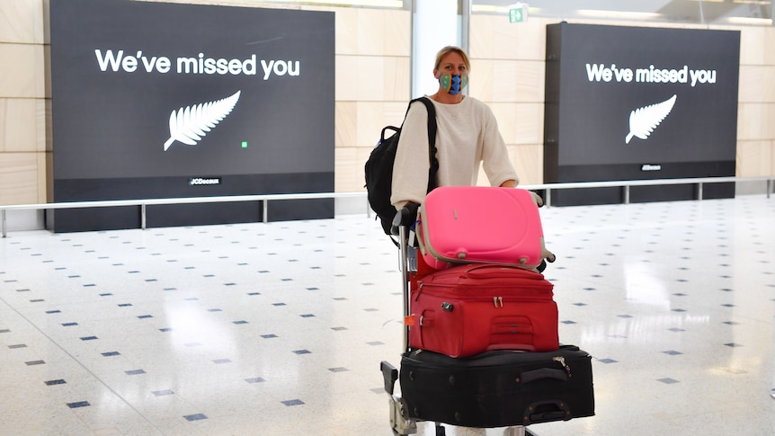 A woman pushes a trolley of luggage at an airport.