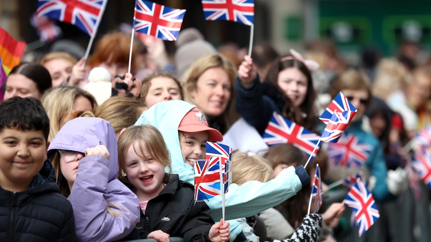 A crowd of people of mixed ages smiling and waving the British flag