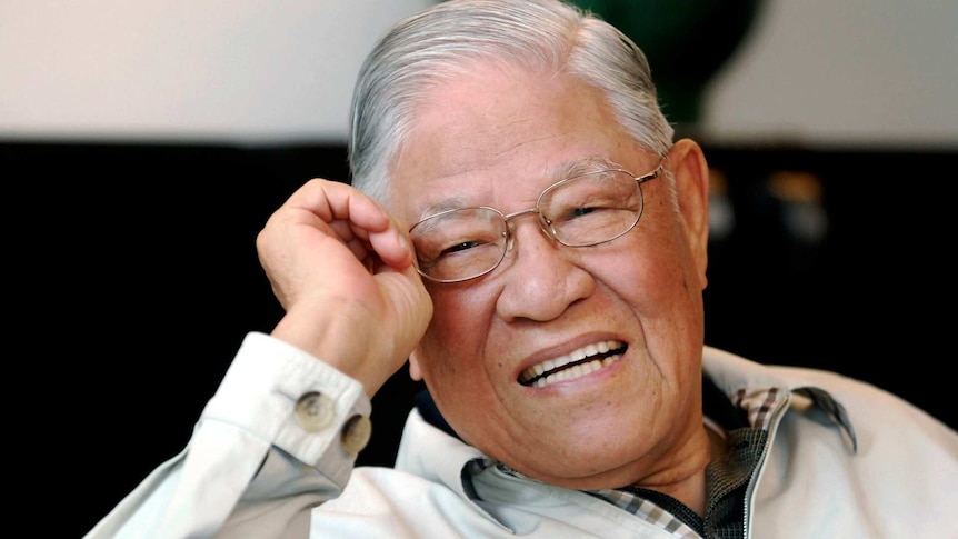 Lee Teng-hut holds his glasses as he smiles and looks off camera