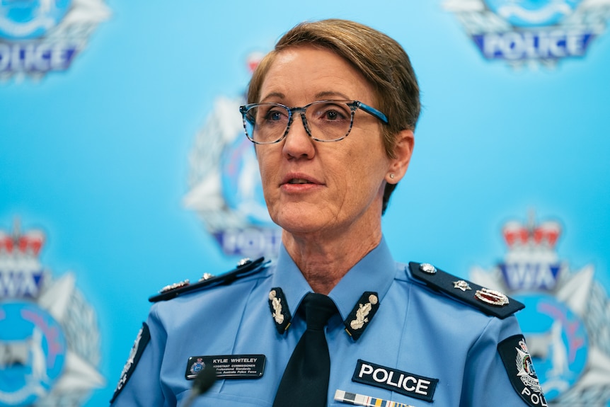 A close up of Kylie wearing a police uniform, standing in front of a wall with WA Police logos on it, at a press conference