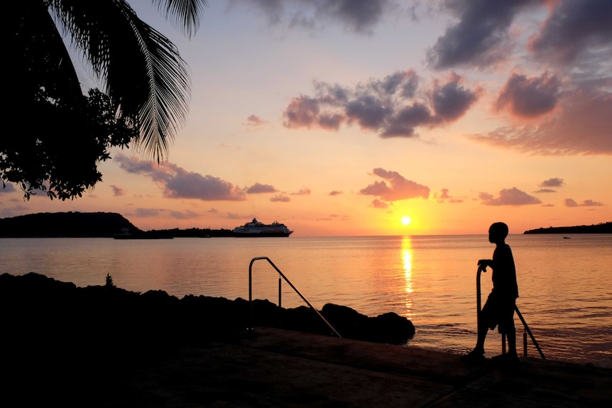 A unset image looking over the water, with a silhouette of a person looking at the view