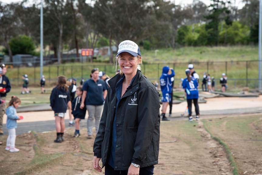 A blonde woman smiles at the camera as she stands around flood damaged hockey grounds.