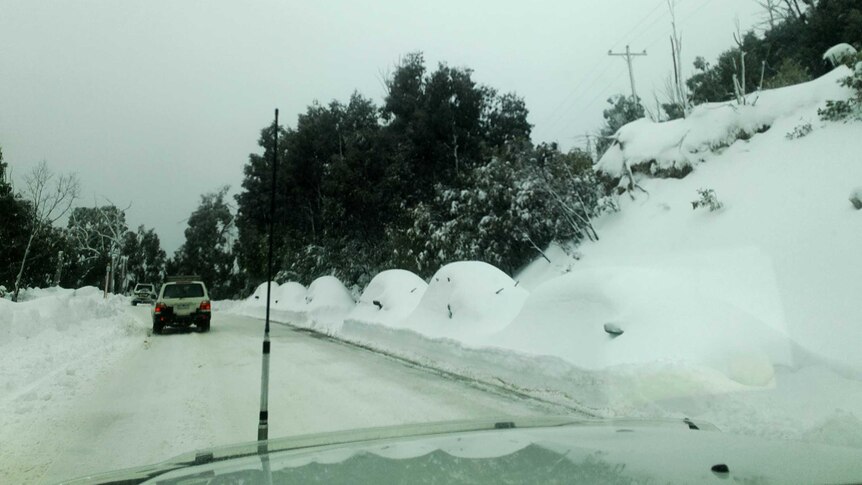 mounds of snow above cars along a road