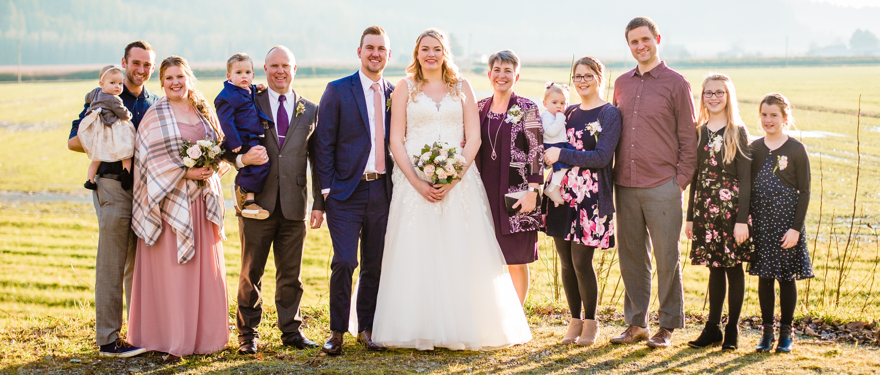 A large family poses for a wedding photo in front of a yellow field