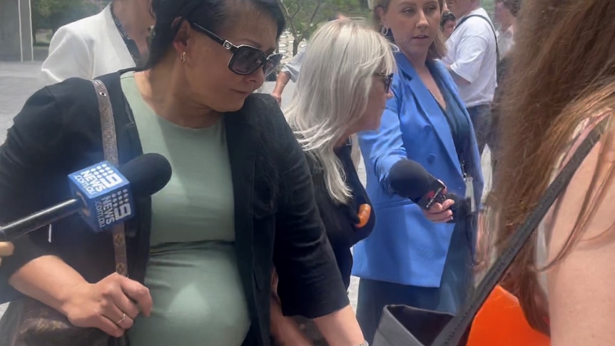 A woman walks into court surrounded by people and media.