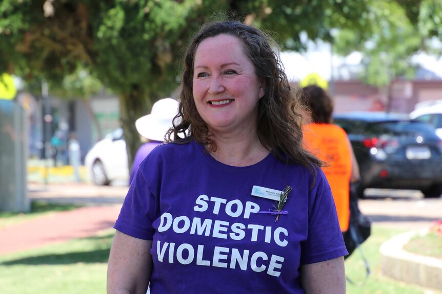 A smiling woman wearing a purple shirt with the words 'stop domestic violence'.