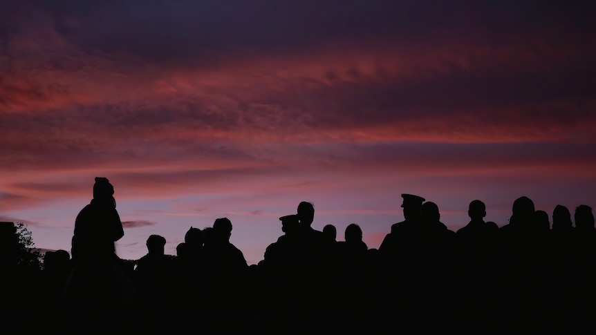 A silhouette of people against a pink sunrise.
