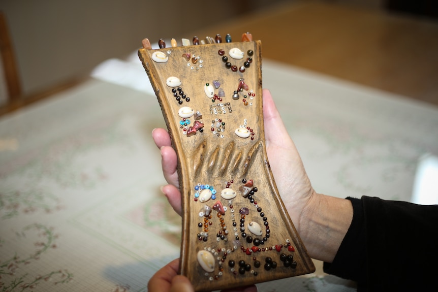 A small wooden board with beads and stones attached.