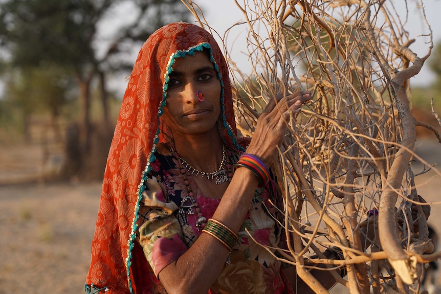 A woman in a red veil holds a bundle of sticks