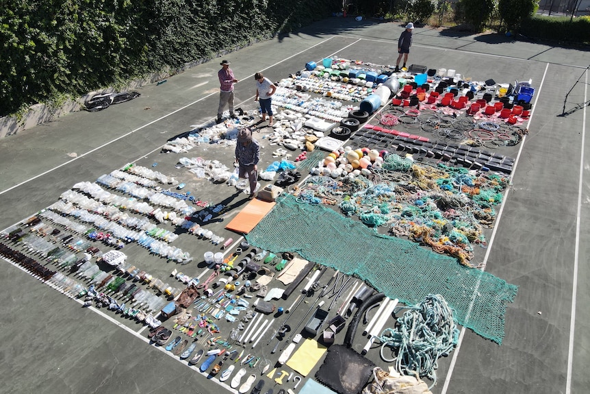 People surrounded by rubbish laid out on a tennis court.