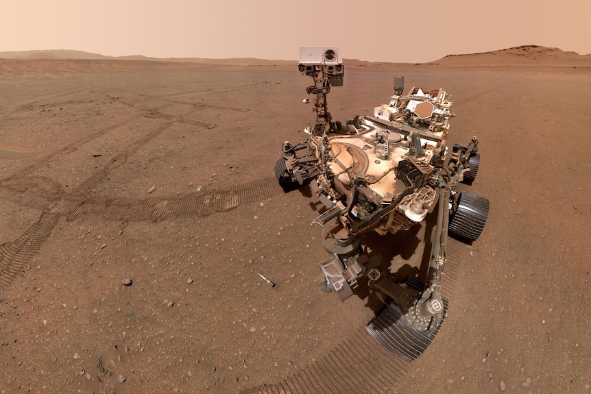 NASA's Perseverance rover appears on the surface of Mars. Tracks and sample tubes are visible in the soil. 