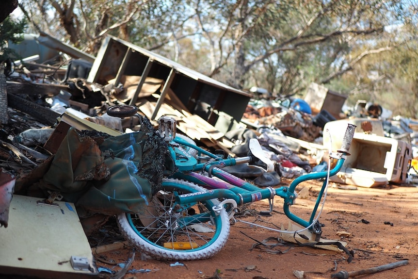A blue children's bike lies on it's side amongst a pile of rubbish dumped in a park.