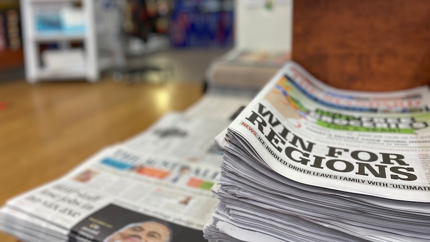 A stack of newspapers in a newsagency with the headline 'win for regions' in foreground