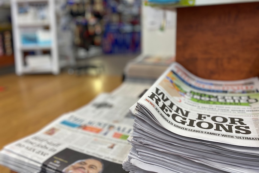 A stack of newspapers in a newsagency with the headline "Win for regions".
