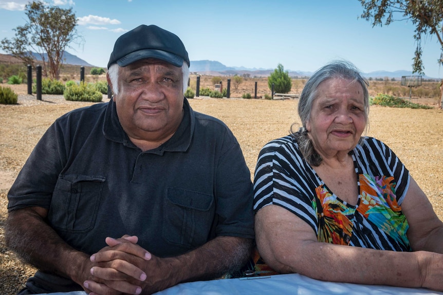 Malcolm 'Tiger' McKenzie and Angelina Stuart sitting at a table outside, with open country behind them