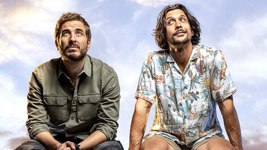 Two actors (Ryan Corr and Bob Morley) sitting on a ledge looking off into the distance, one in khaki green, the other in colours