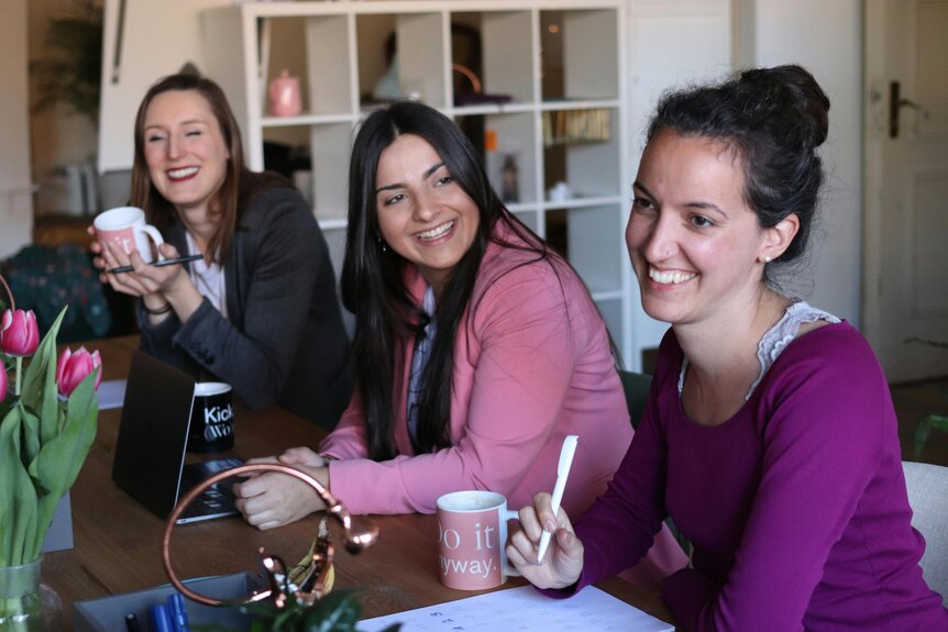 three women chatting and smiling at computer desk