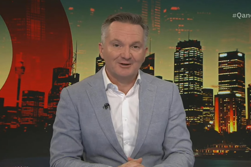 Chris Bowen against a Q+A backdrop wearing a pale grey suit.