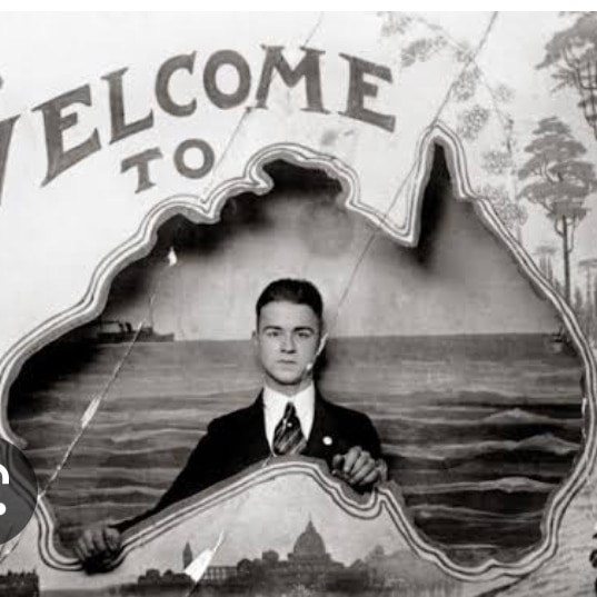 Migrant from Greece looking through a cut-out sign in the shape of Australia with a title 'welcome'