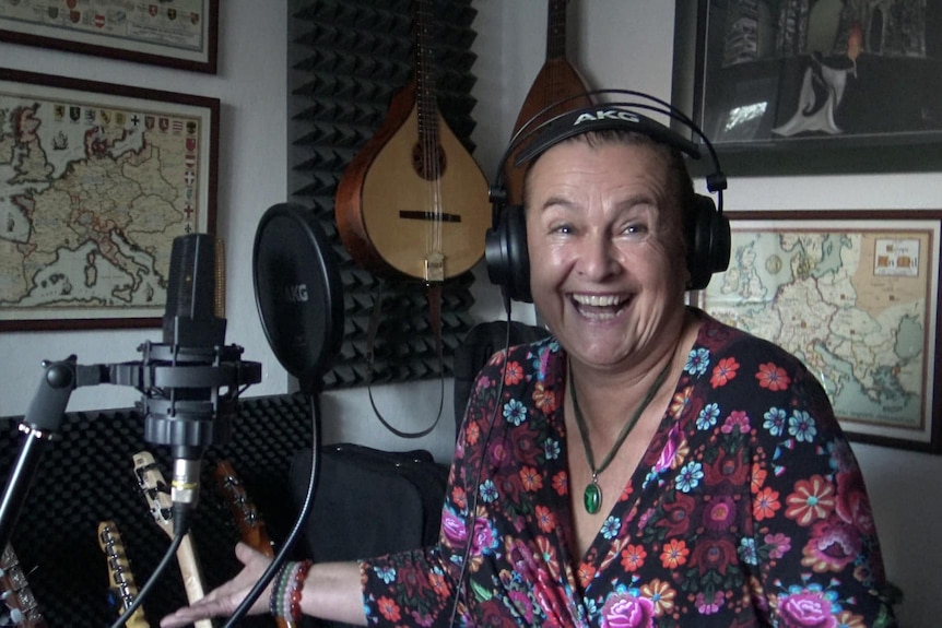 A woman in a recording studio is smiling and has headphones on her ears.