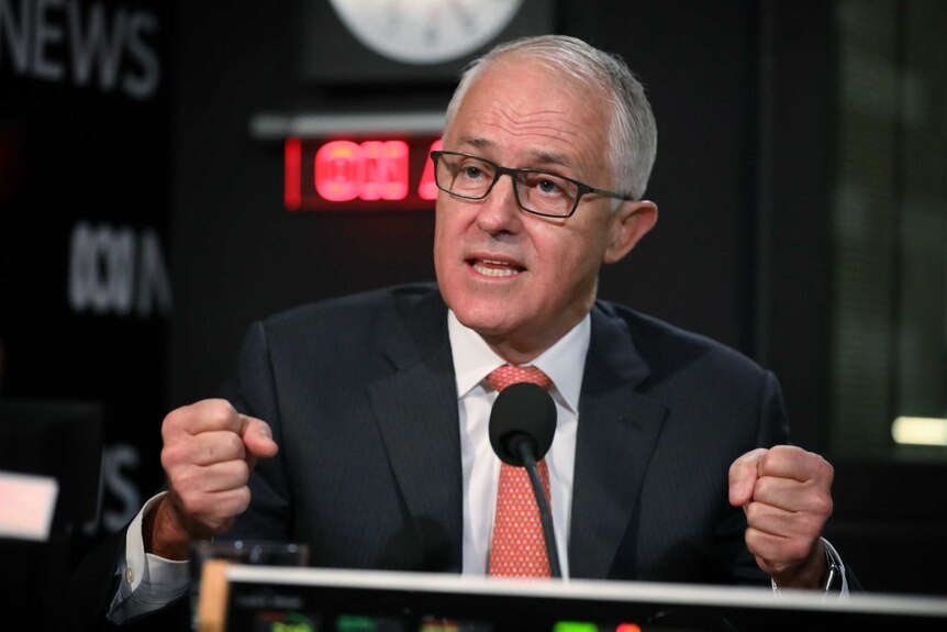 Malcolm Turnbull curls both hands into fists, raises his eyebrows while speaking into a microphone in a radio studio.