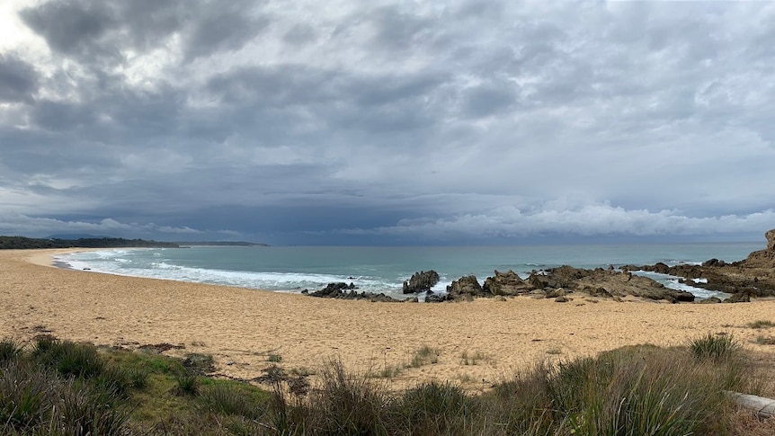 dark clouds gather off the shore of a beach, where waves are rolling onto the shore