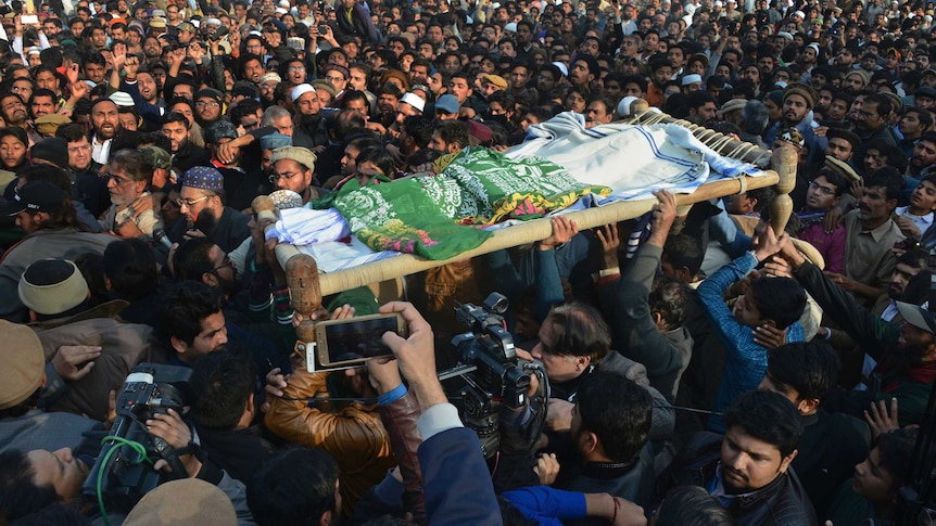 Large crowd hold up body under green and white cloth on a stretcher