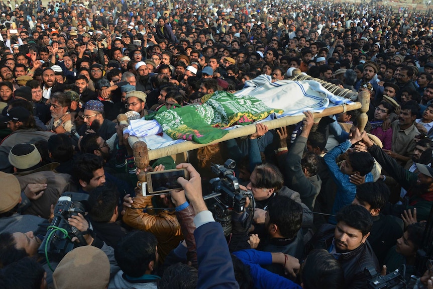 Large crowd hold up body under green and white cloth on a stretcher