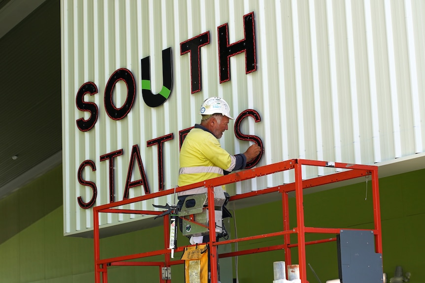 A man stands on an elevated platform and installs signage