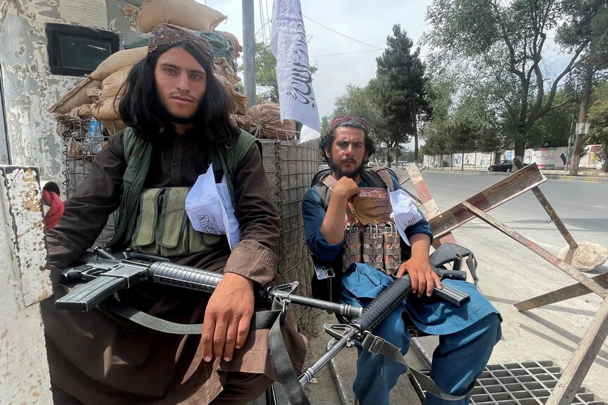 Two members of Taliban forces sit at a checkpost in Kabul with guns on their lap.