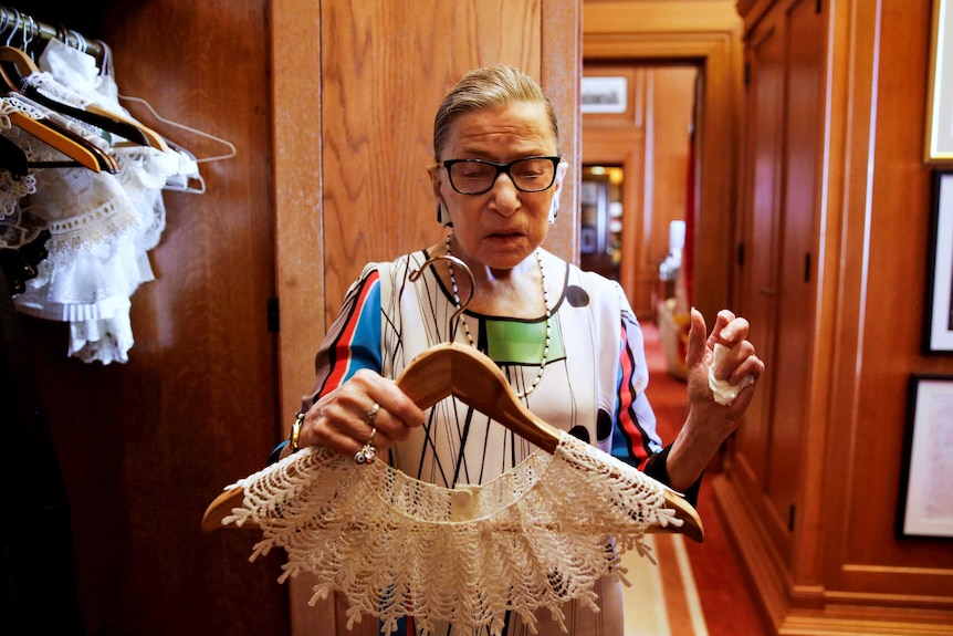 Ruth Bader Ginsburg holding up a white lacy collar on a coat hanger