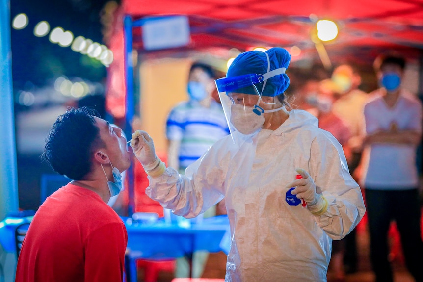 A woman in full PPE sticks a swab down a man's throat 