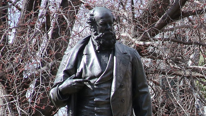 Raised bronze statue of William Crowther with his hand on his chest, in the centre of park in Hobart city