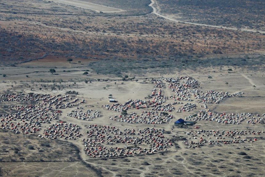 An aerial view of a large group of small white tents or huts in a dry landscape.