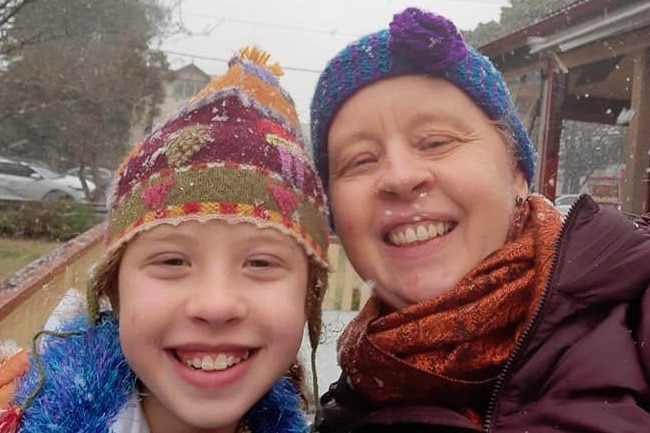 A young girl and a woman smile at the camera.