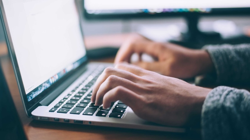 A man's hands type on a laptop.