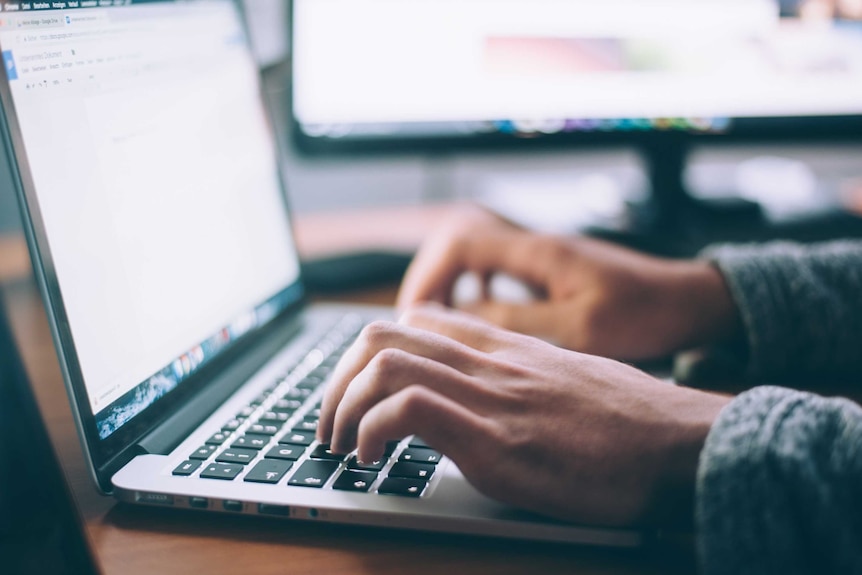 A man's hands type on a laptop.