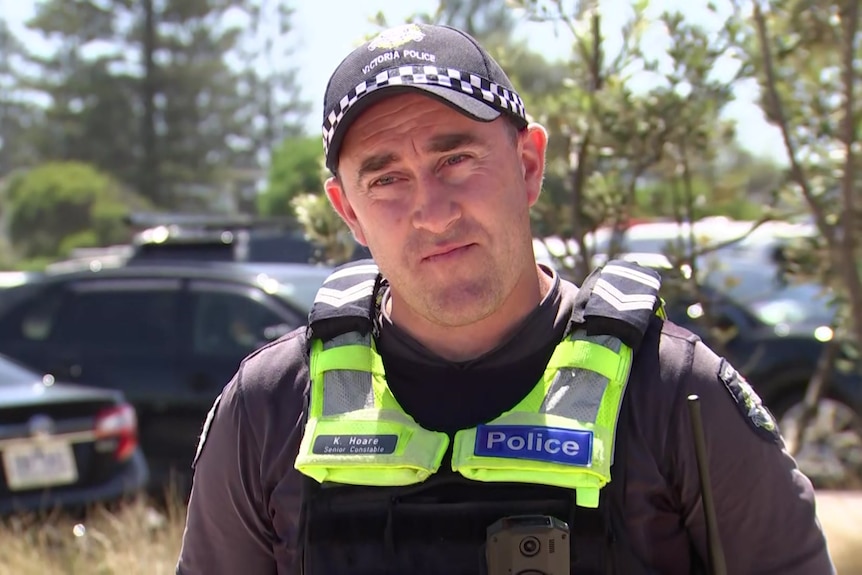 Senior Constable Kevin Hoare wears a police cap and fluro yello vest and stands in a carpark.