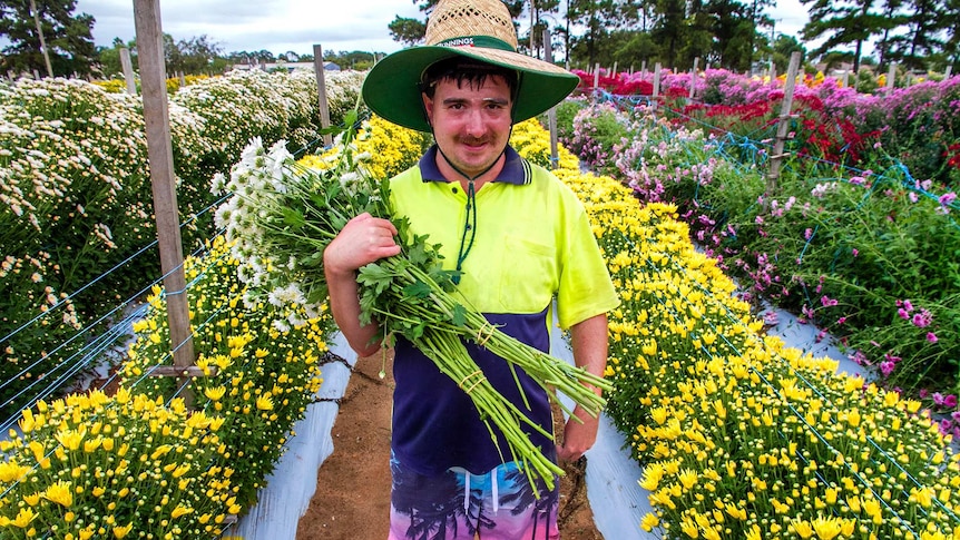 A man holds a bunch of cut flowers in a flower field.
