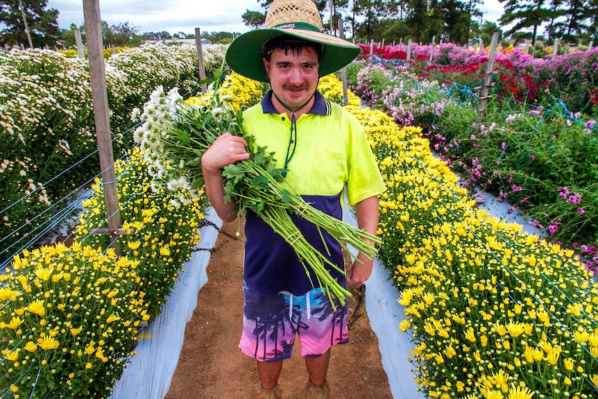 A man holds a bunch of cut flowers in a flower field.