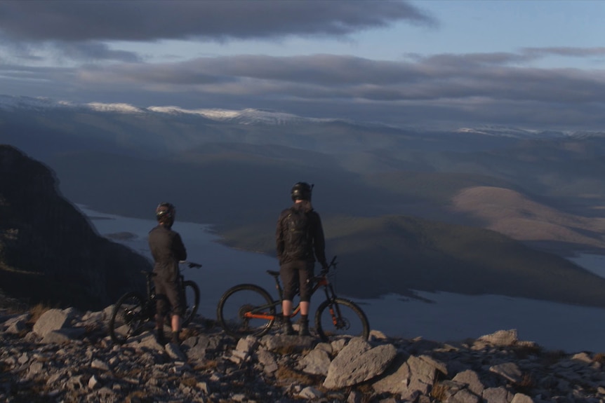 Two mountain bikes stop to enjoy epic mountain top view over western Tasmania