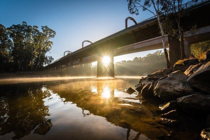 A wide shot of the Echuca Moama bridge at Sunset, the bright light reflects off the water and bridge is in shadown