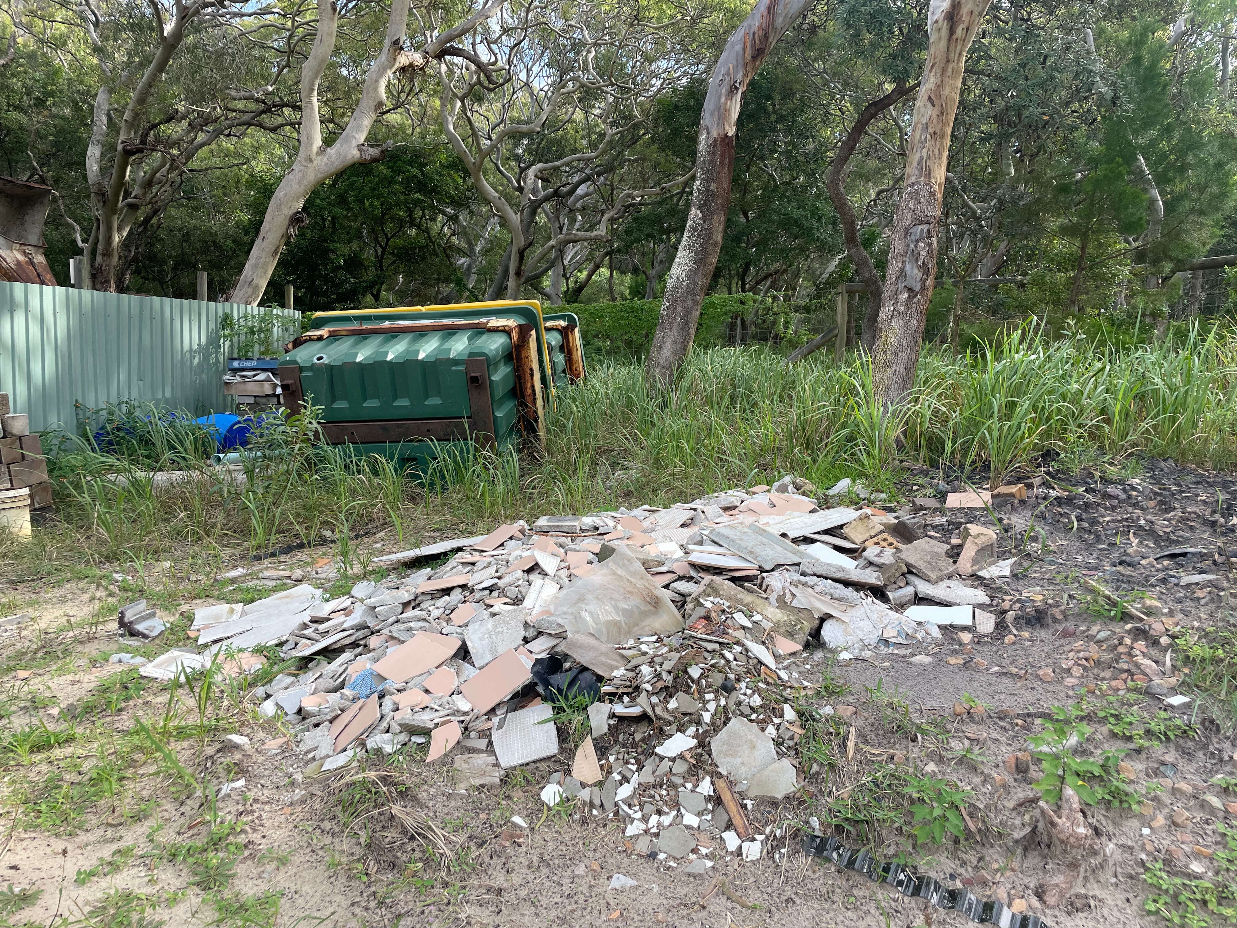 Landfill and large tip bins surrounded by green trees and shrubs.