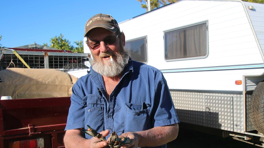 Jeff Seawright in blue shirt and cigarette in his mouth, holding a yabby.